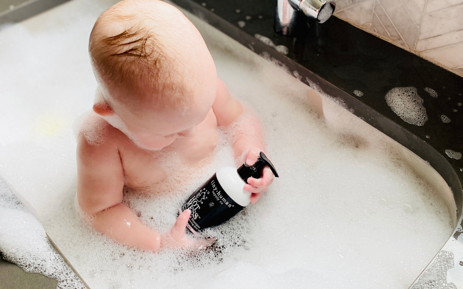 baby in bubble bath holding tiny human supply hot mess baby soap and shampoo 
