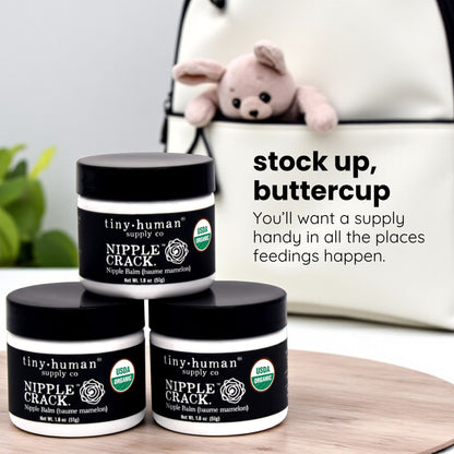 Three jars of tiny-human nipple crack balm on a wooden surface with a plush toy in the background.