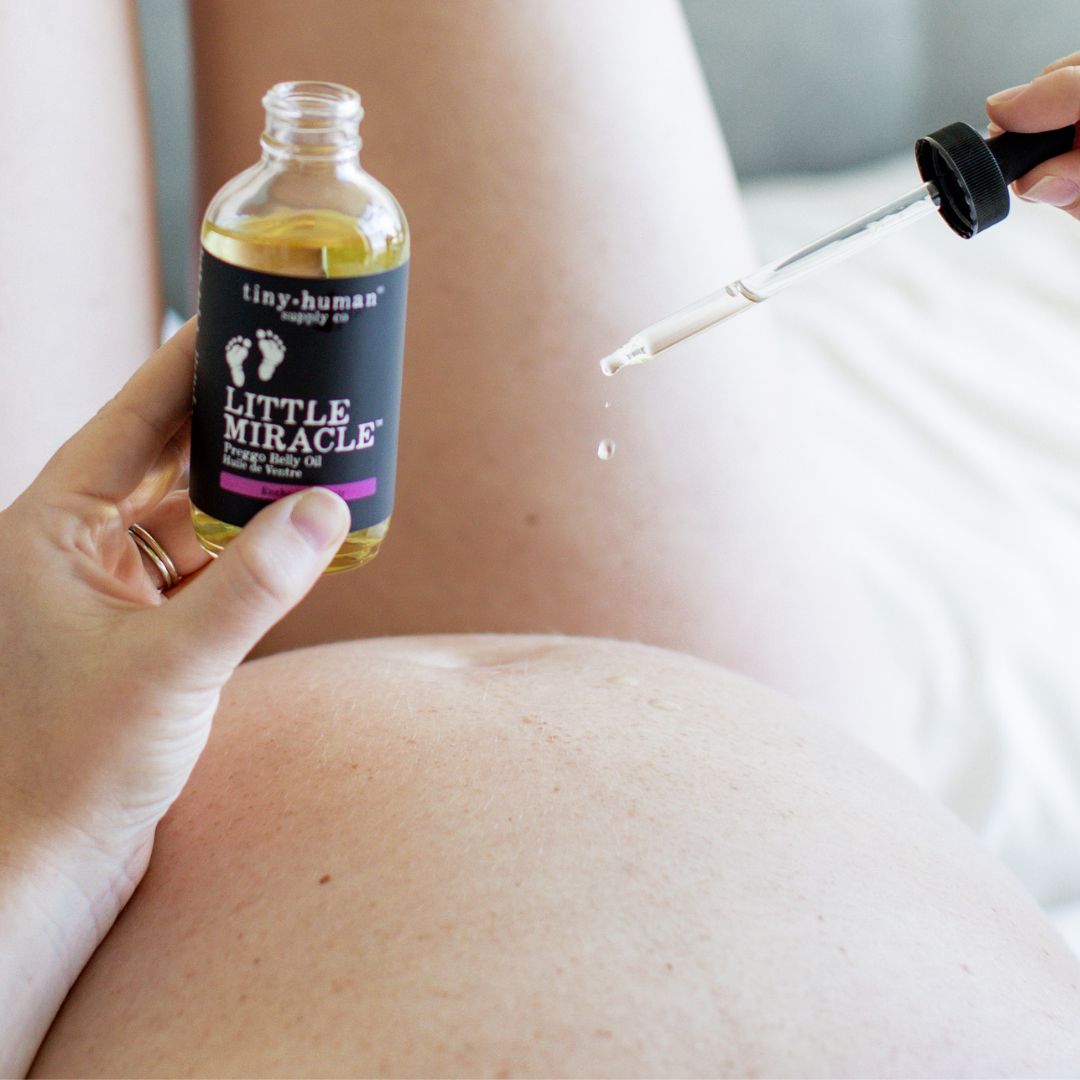 pregnant mom applying tiny human supply organic little miracle belly oil to pregnant stomach